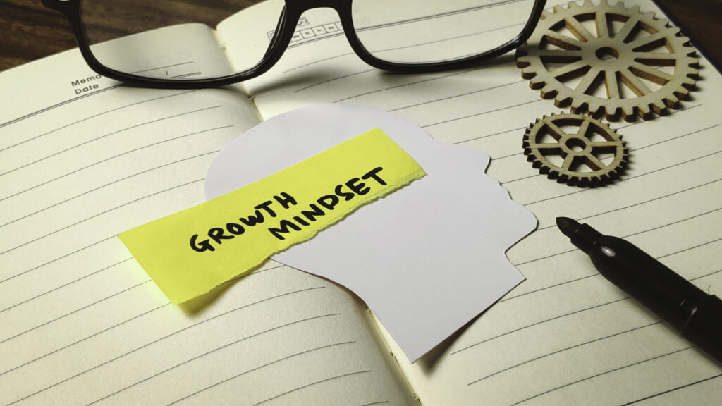 A notebook and gears with a sticky note, illustrating how to develop a growth mindset.