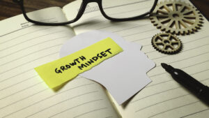 A notebook and gears with a sticky note, illustrating how to develop a growth mindset.